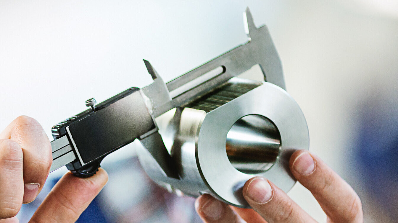 Ein Mann vermisst ein Bauteil aus Edelstahl mit einer Schieblehre